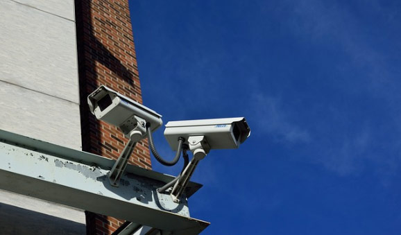 Two security cameras mounted on a building exterior under a clear blue sky.