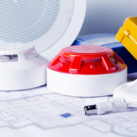 A variety of fire safety equipment, including a red smoke detector, alongside technical blueprints on a white surface.