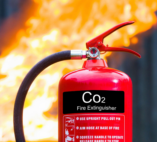 A co2 fire extinguisher ready for action with flames in the background.