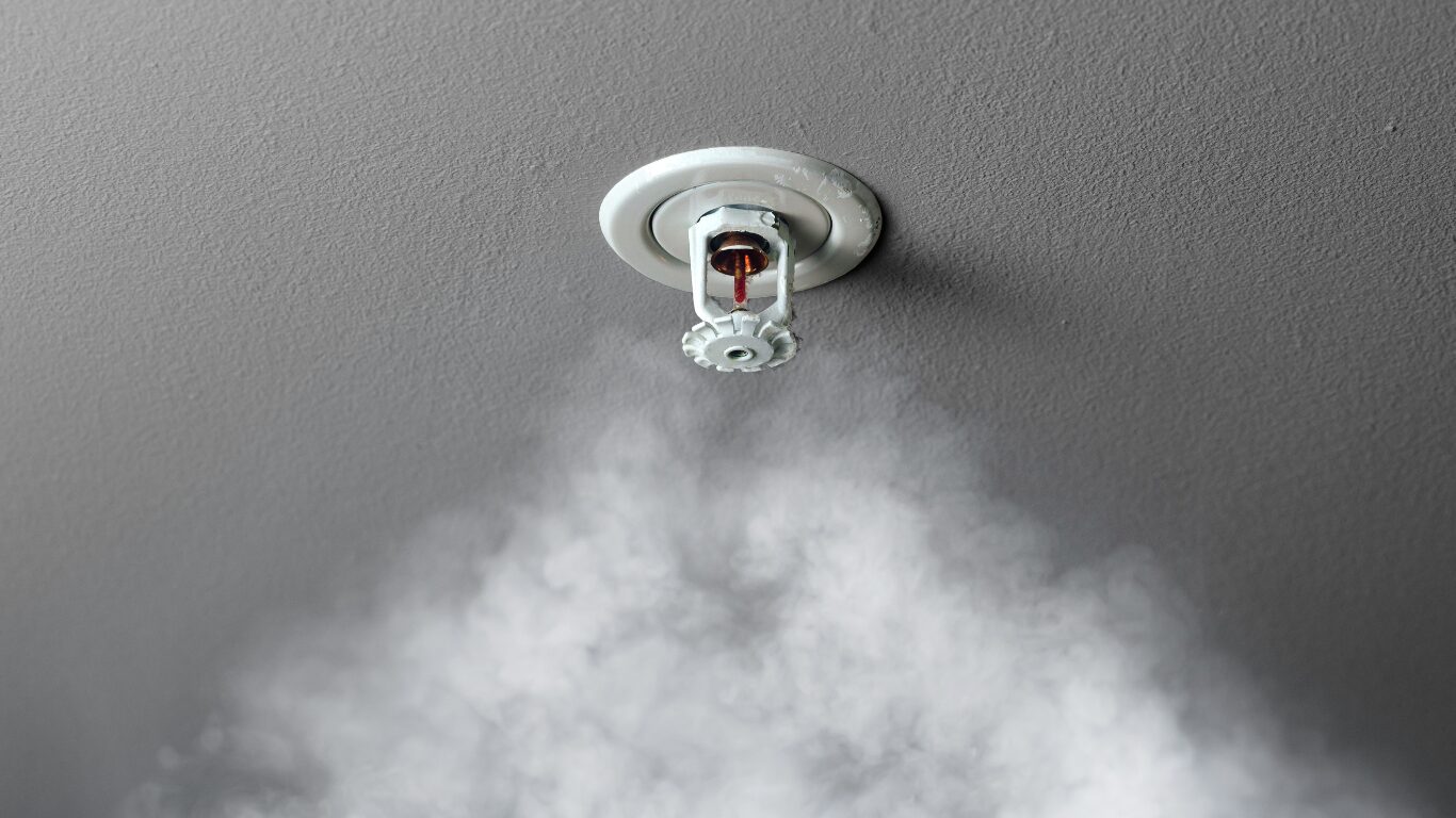 Fire sprinkler on the ceiling of a room with smoke underneath it