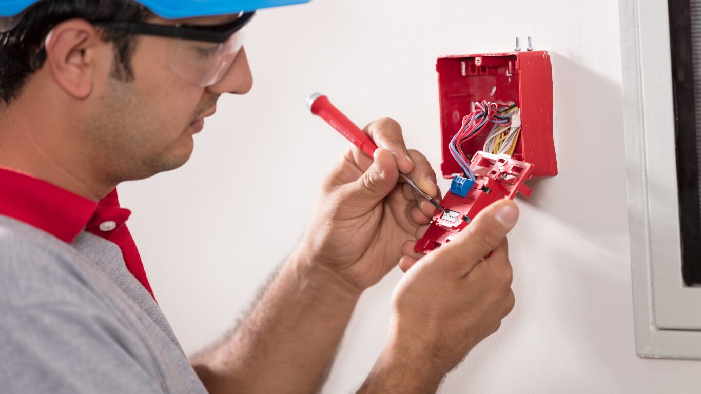 UK fire safety professional installing a fire alarm into the wall.