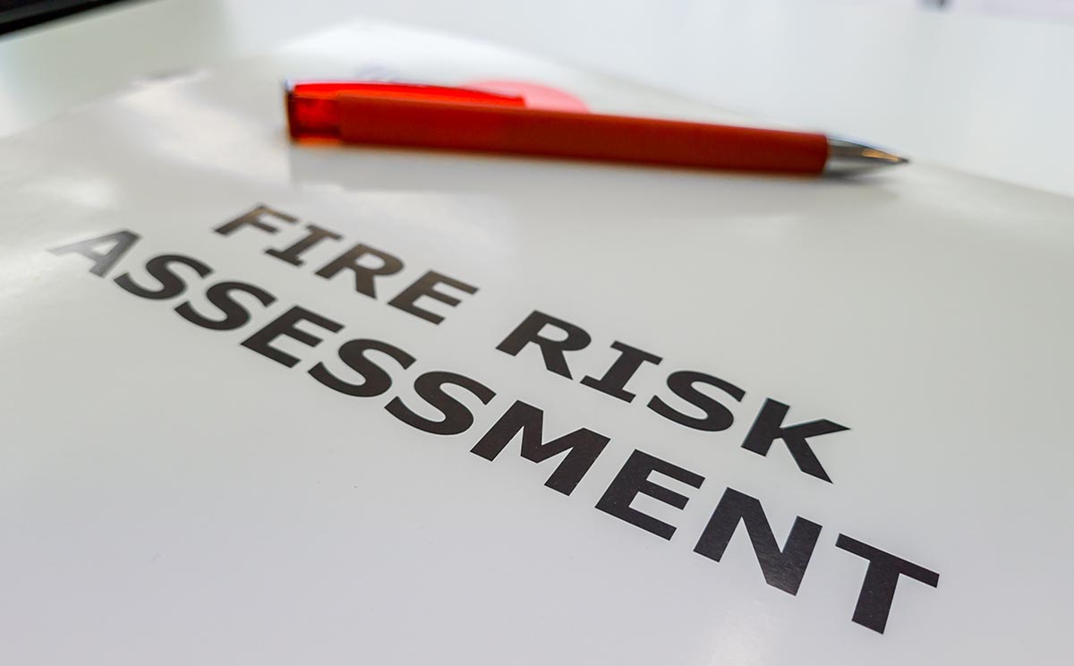 A white file containing the fire risk assessment inside of it and a red pen on top of the file.