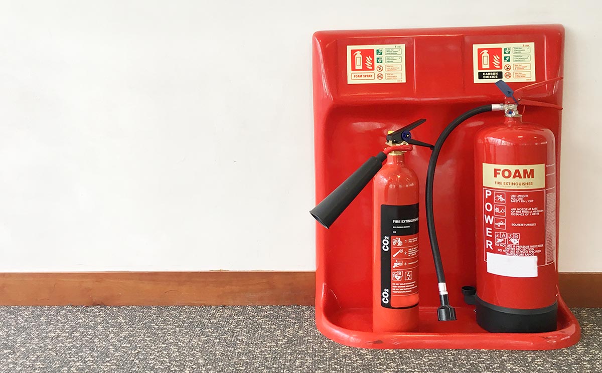 A foam and co2 fire extinguisher installed to the wall of a businesses property, along the hall way.