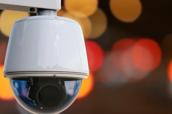 Close-up of a commercial dome security camera with blurred lights in the background.