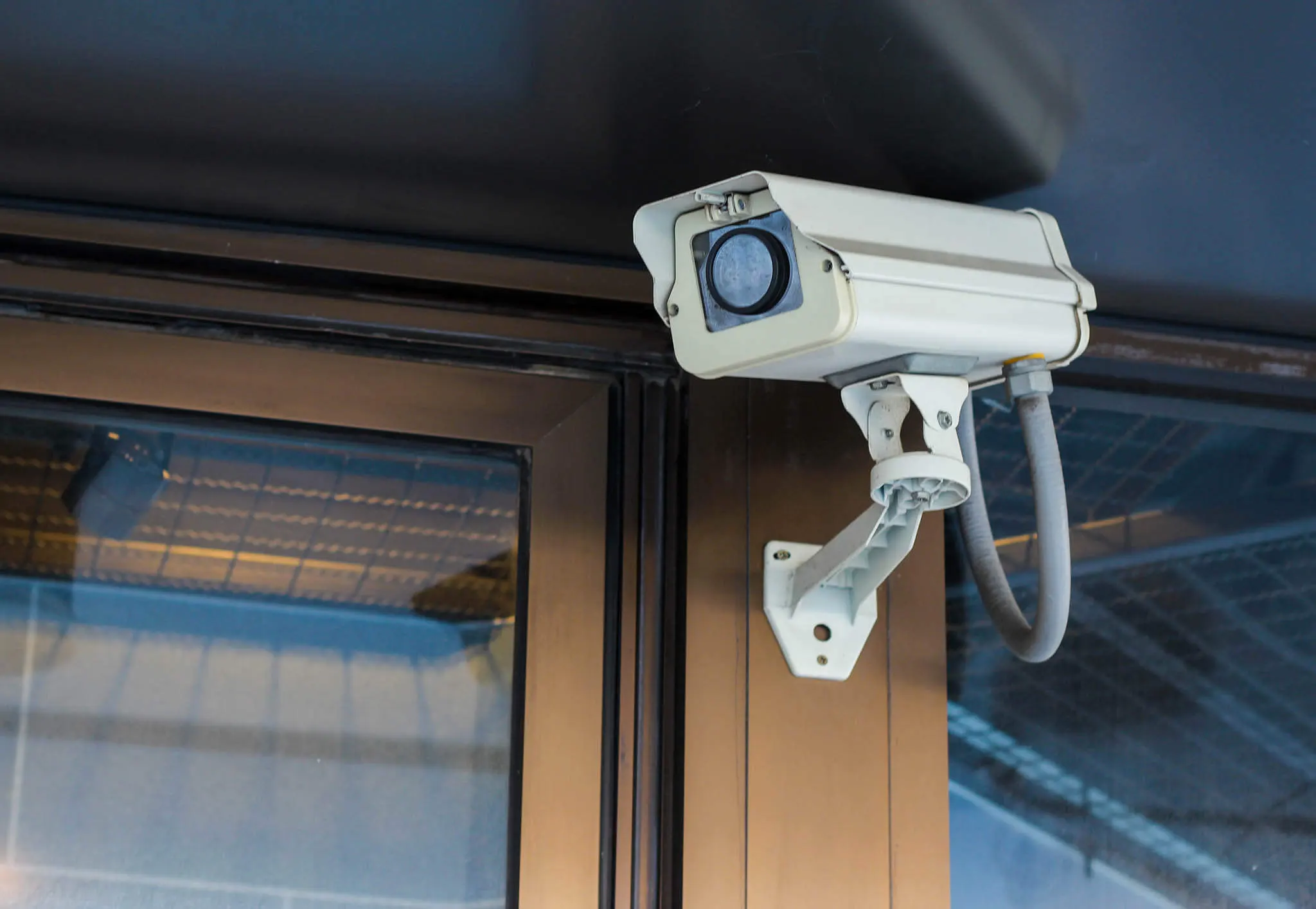 A commercial CCTV camera mounted on the exterior of a business building, positioned above a window.